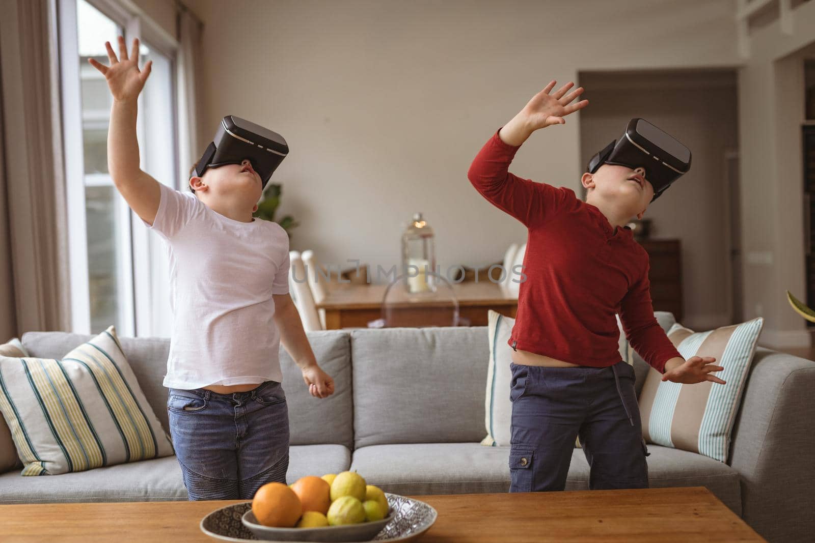 Two caucasian boys wearing vr headsets gesturing in the living room at home. gaming and entertainment concept