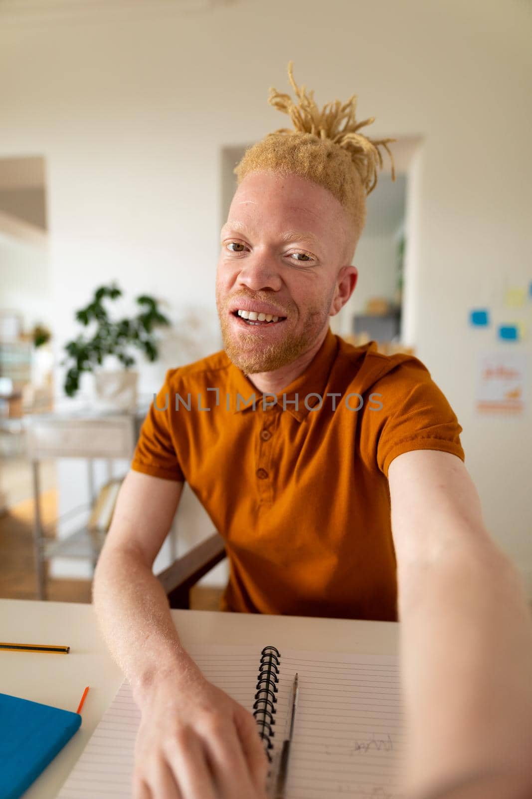 Portrait of happy african american man with dreadlocks working from home. remote working using technology at home.