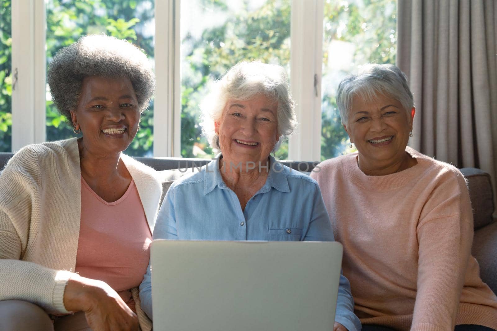 Three happy diverse senior woman sitting on sofa and using laptop. retirement lifestyle relaxing at home with technology.