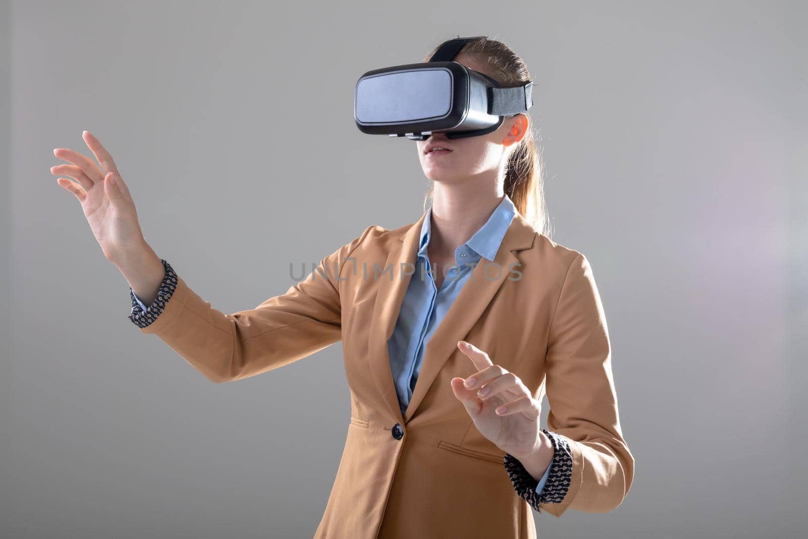Caucasian businesswoman wearing vr headset touching virtual interface, isolated on grey background by Wavebreakmedia