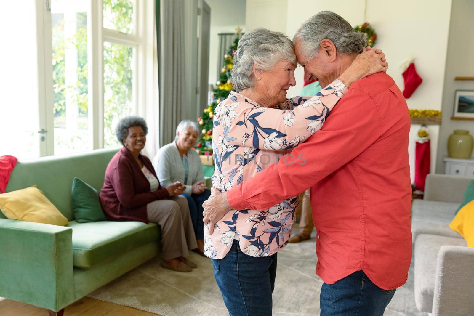 Happy caucasian senior couple dancing in front of their diverse friends at christmas time. christmas festivities, celebrating at home with friends.
