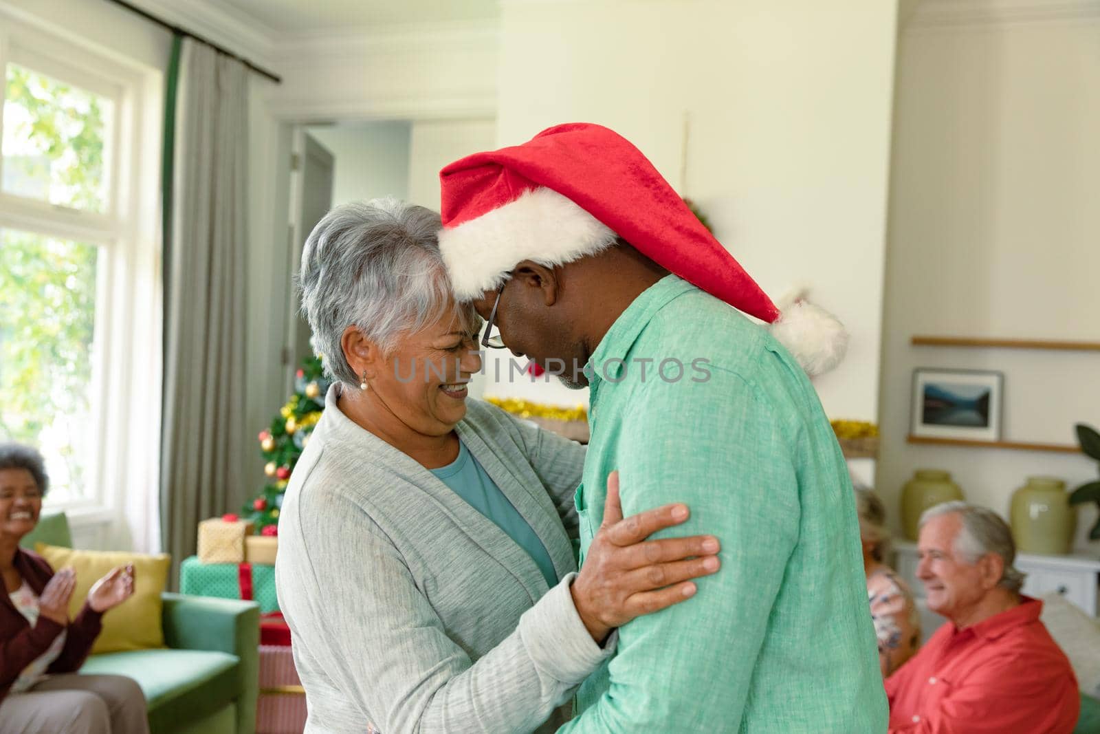 Happy diverse senior couple dancing in front of their diverse friends at christmas time. christmas festivities, celebrating at home with friends.