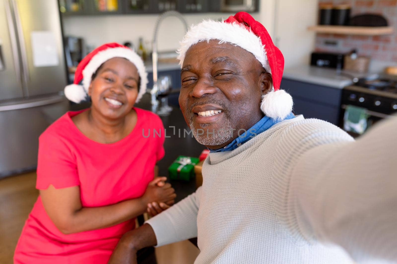 Happy african american senior couple taking selfie in kitchen at christmas time. retirement lifestyle, christmas festivities and communication technology.