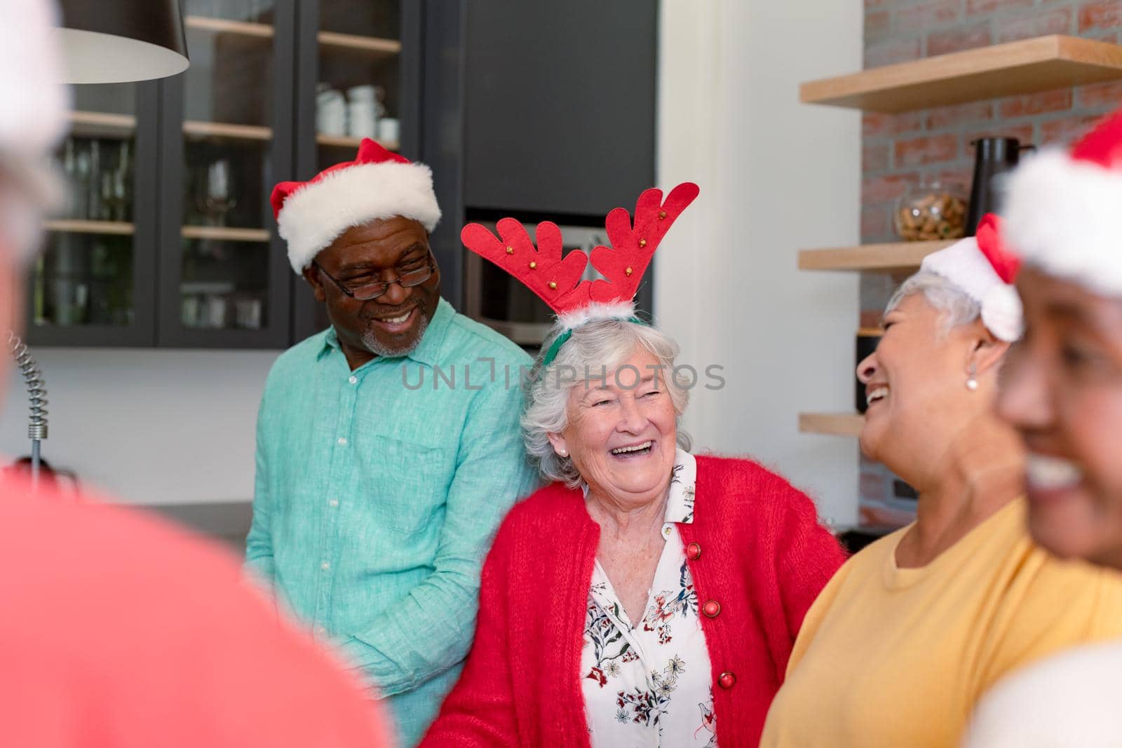 Group of happy diverse senior male and female friends in christmas hats cooking together in kitchen. christmas festivities, celebrating at home with friends.