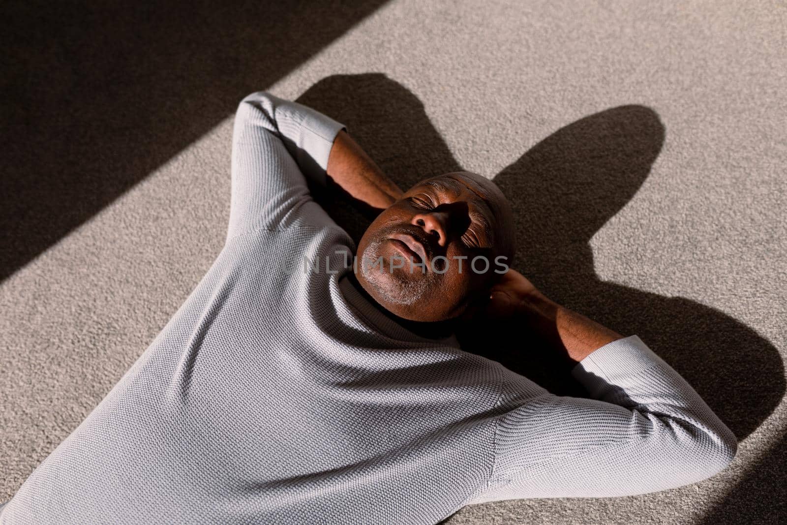 Relaxed african american senior man lying on floor in ray of light. retirement lifestyle, spending time at home.
