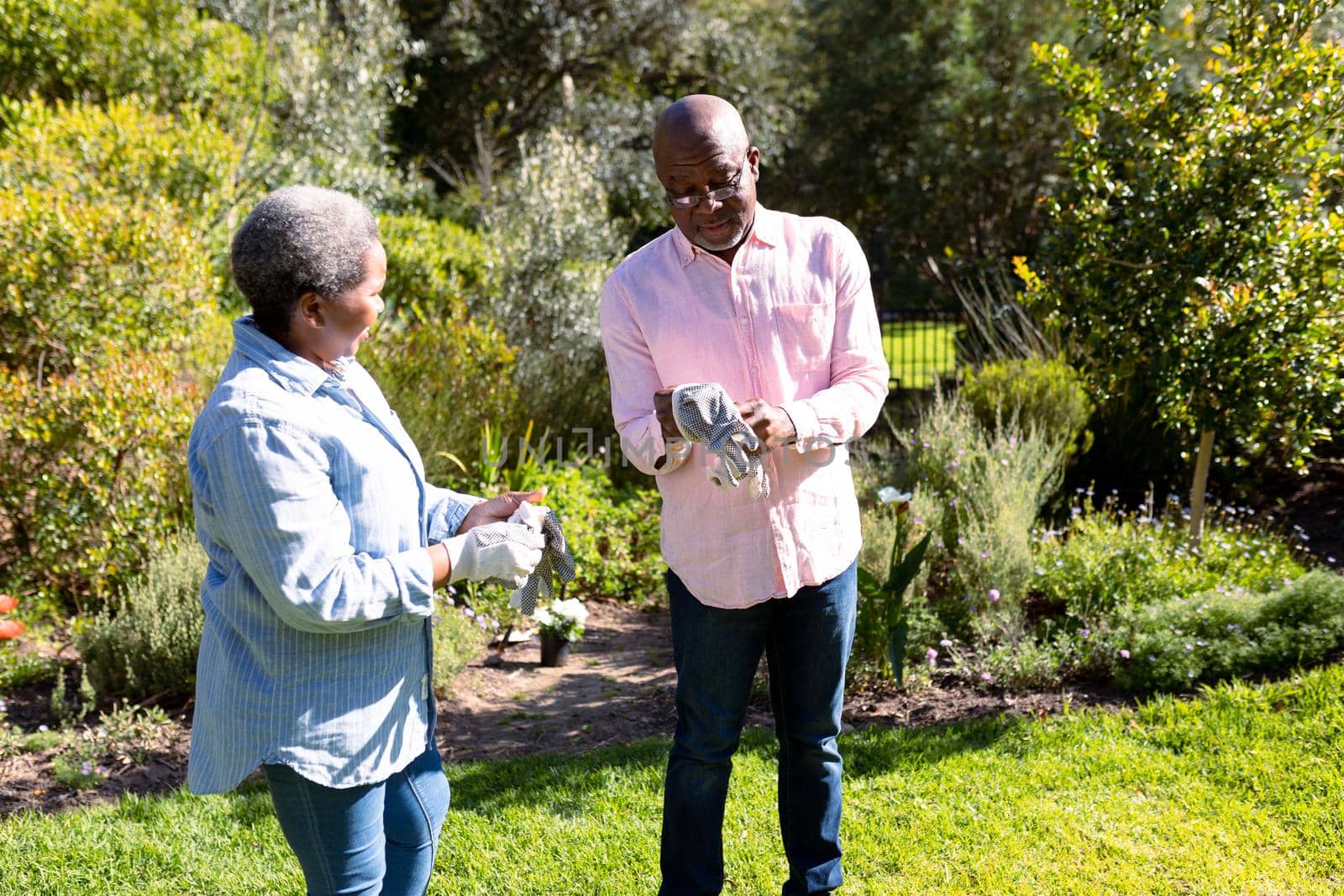 African american senior couple gardening, putting on gloves outdoors. retirement lifestyle, spending time at home and garden.