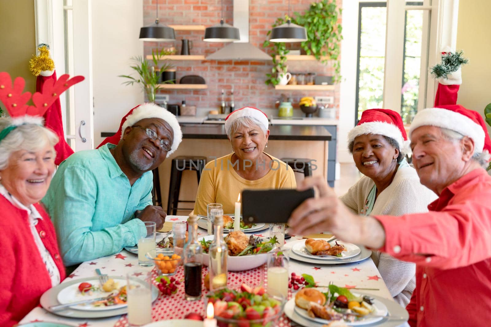 Diverse group of happy senior friends in holiday hats celebrating christmas together, taking selfie. christmas festivities, celebrating at home with friends.