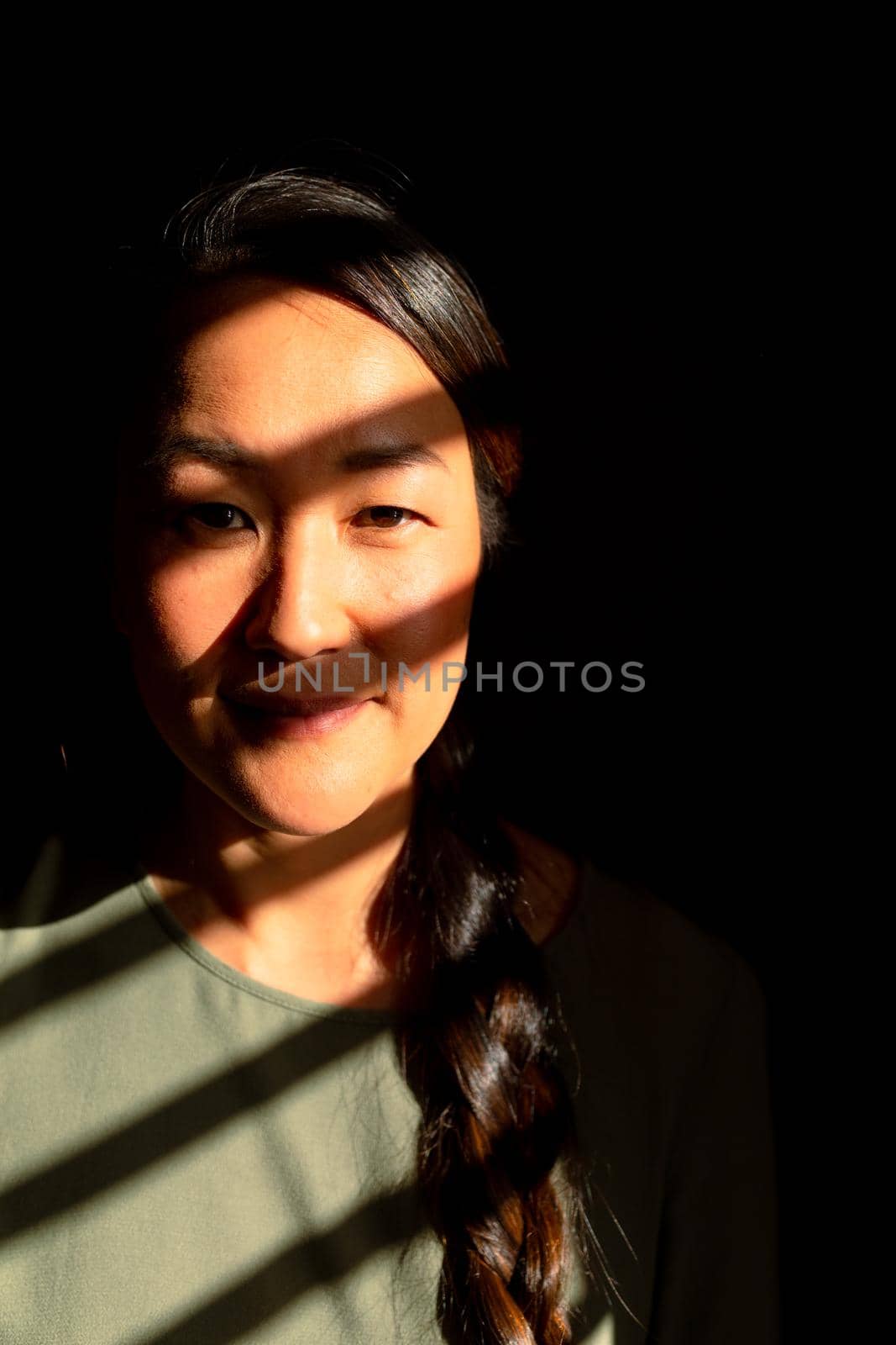 Portrait of serious asian woman standing in ray of light at home by Wavebreakmedia