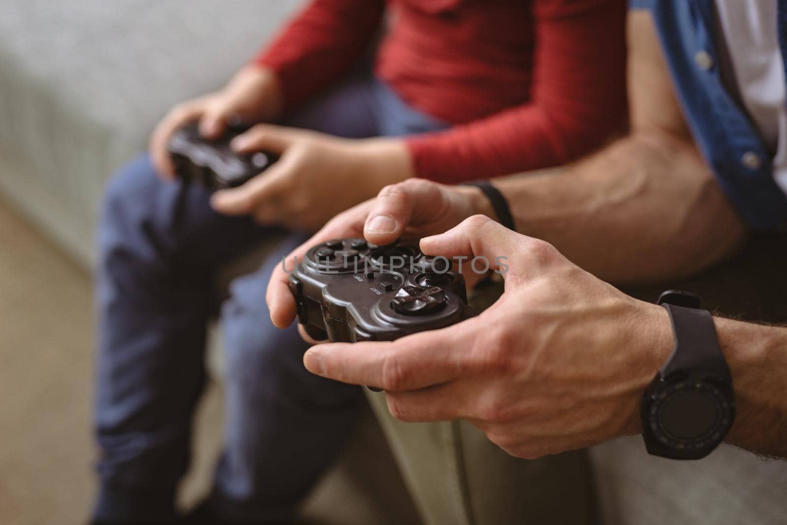 Mid section of caucasian father and son playing video games together sitting on the couch at home. fatherhood and love concept