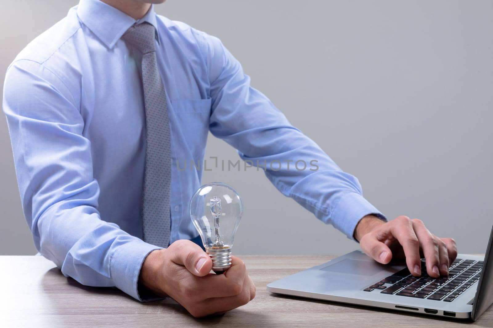 Midsection of caucasian businessman holding light bulb using laptop, isolated on grey background. business technology, communication and growth concept.