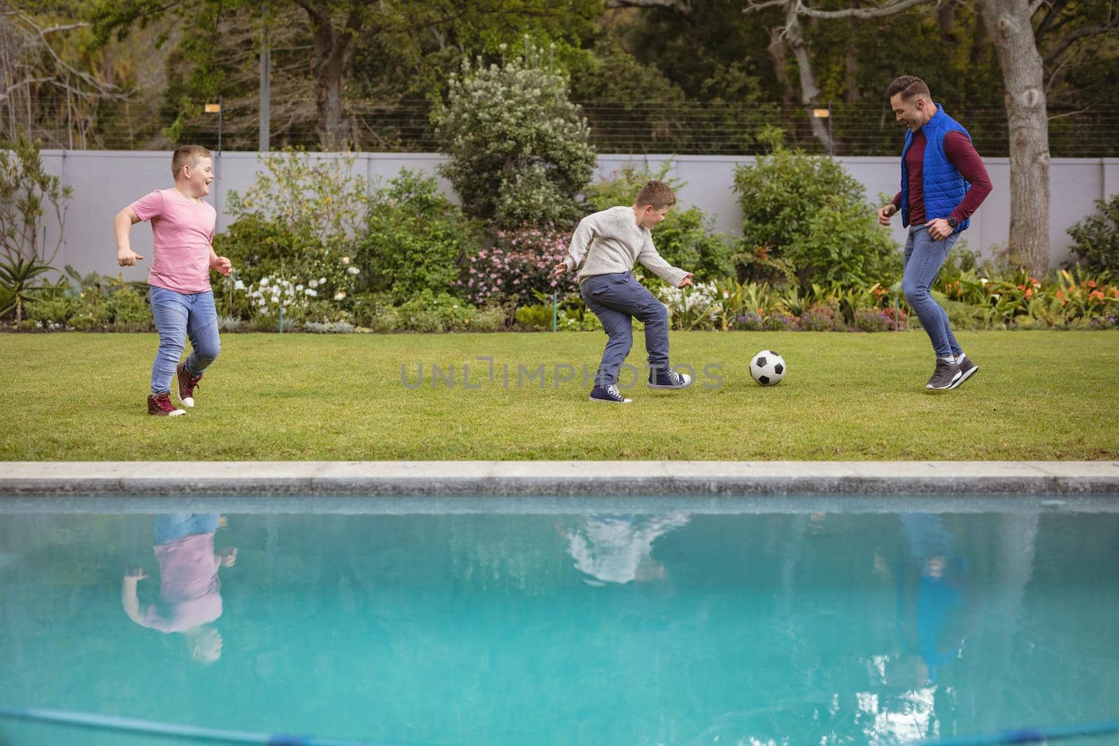 Caucasian father and two sons playing football together in the garden by Wavebreakmedia