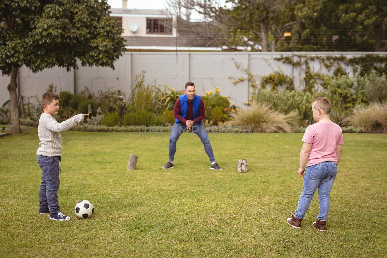 Caucasian father and two sons playing football together in the garden by Wavebreakmedia
