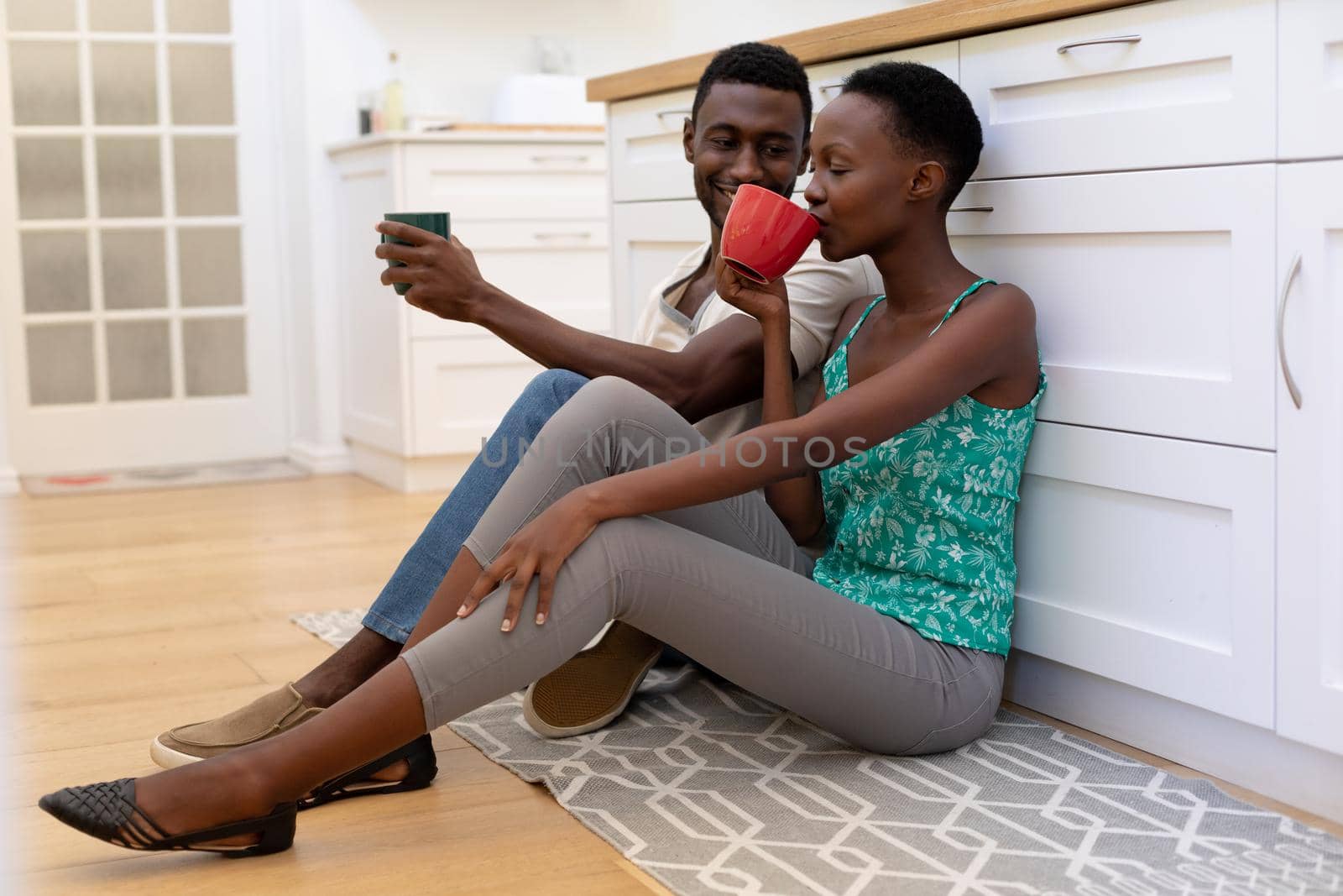 African american couple sitting on floor in kitchen holding mugs by Wavebreakmedia