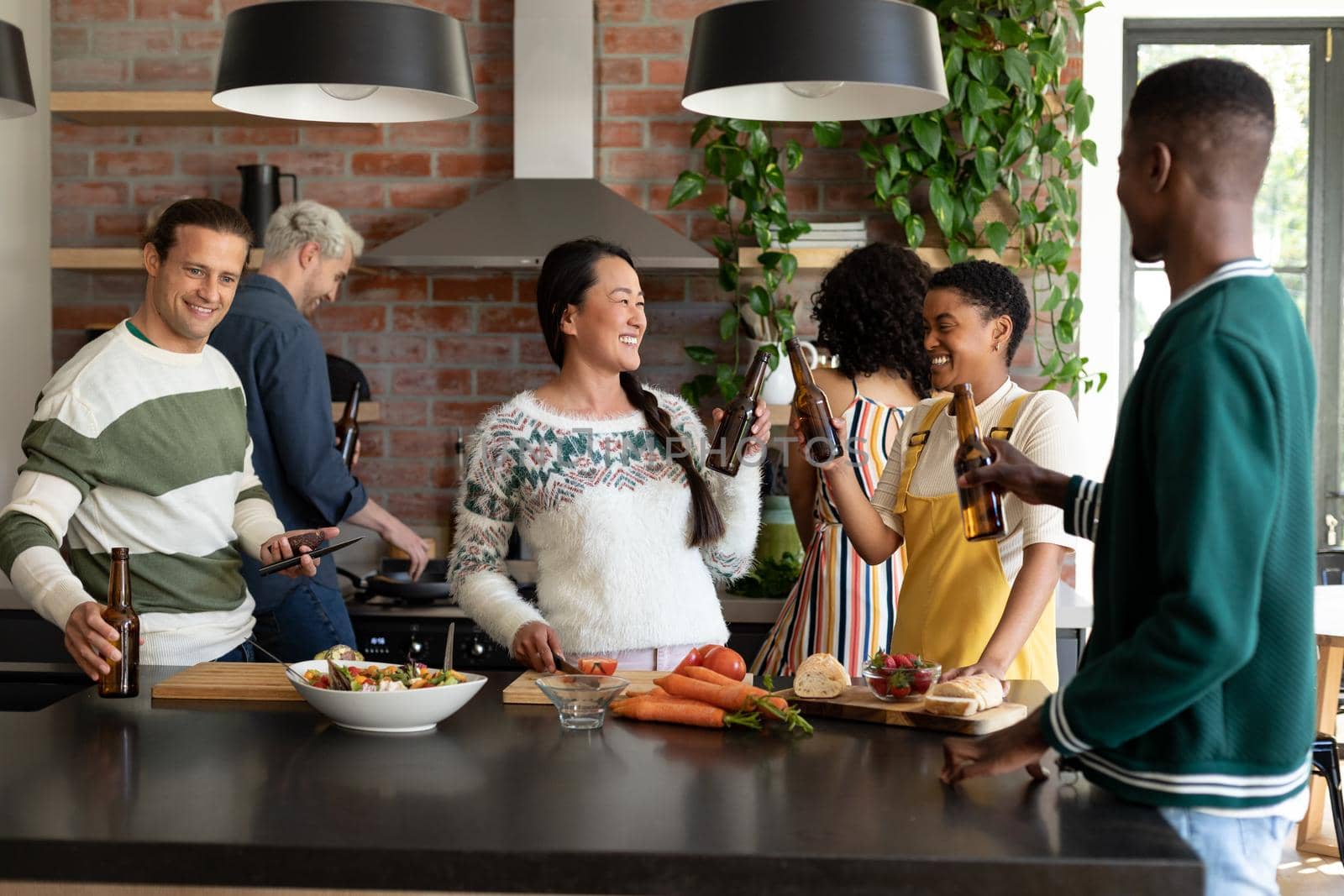Group of happy diverse female and male friends drinking beer and cooking together in kitchen by Wavebreakmedia