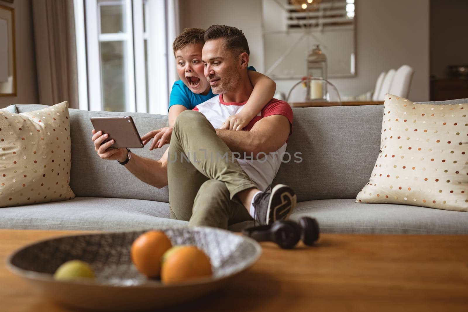 Caucasian father and son using digital tablet on the couch at home. fatherhood, technology and home concept