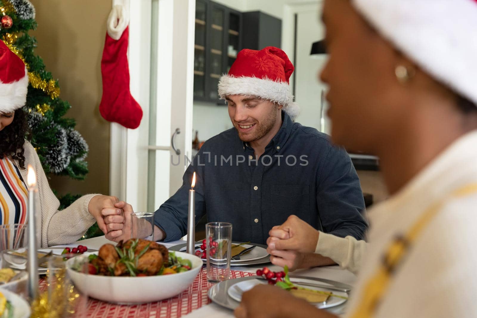 Caucasian man praying with friends at christmas table at home. christmas festivities, celebrating at home with friends