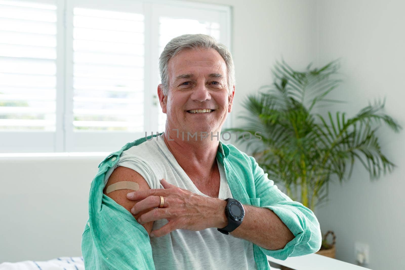 Smiling caucasian senior man with plaster on arm looking at camera after vaccination. senior health and lifestyle during covid 19 pandemic.