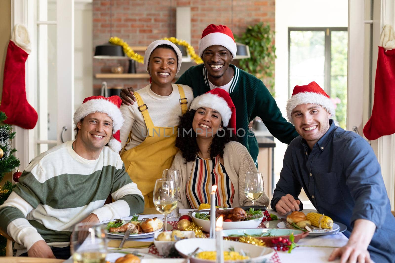 Group of happy diverse female and male friends in santa hats , celebrating christmas, taking photo. christmas festivities, celebrating at home with friends.