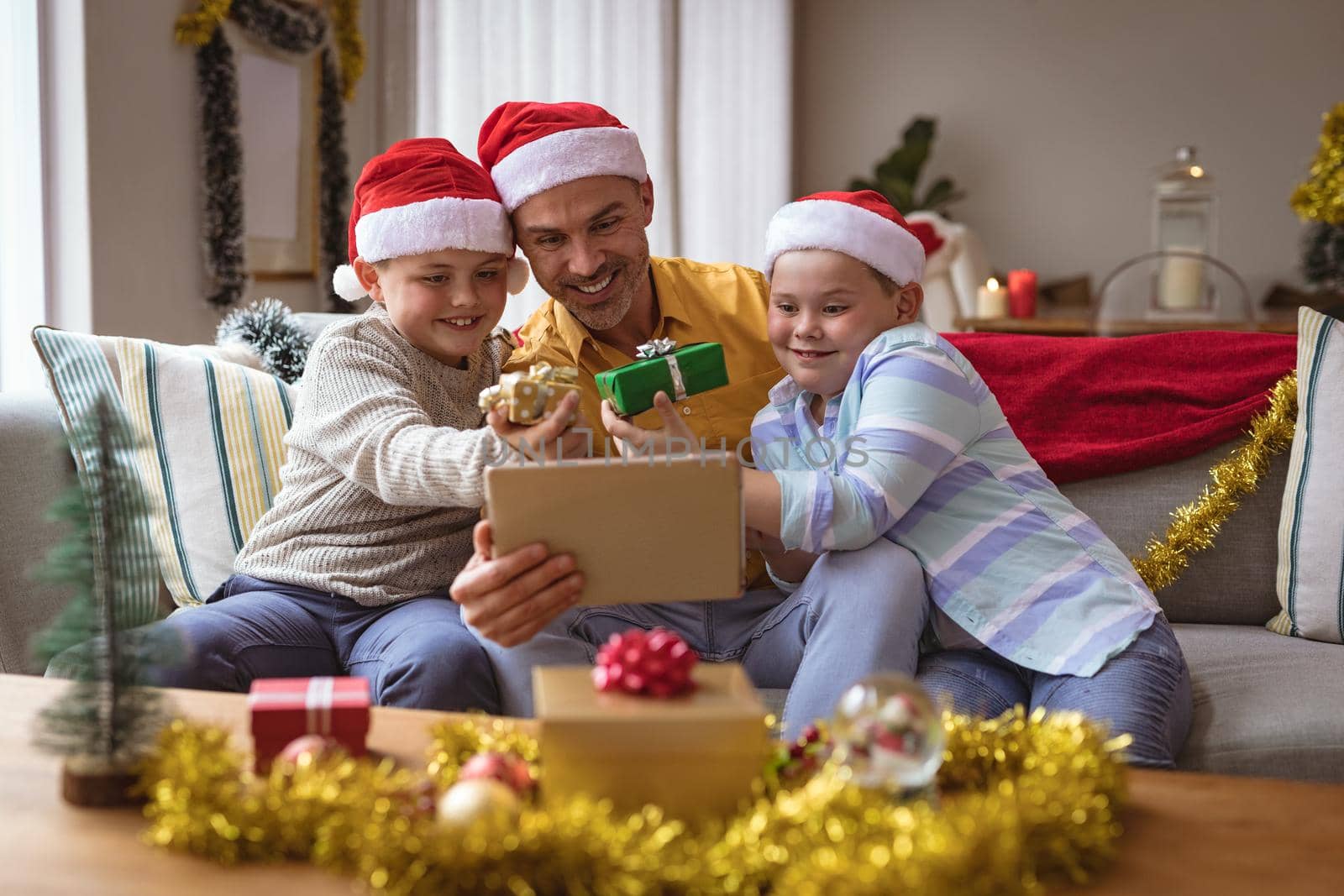 Caucasian father and two sons showing gifts during video call on digital tablet during christmas. social distancing during covid 19 pandemic at christmas time