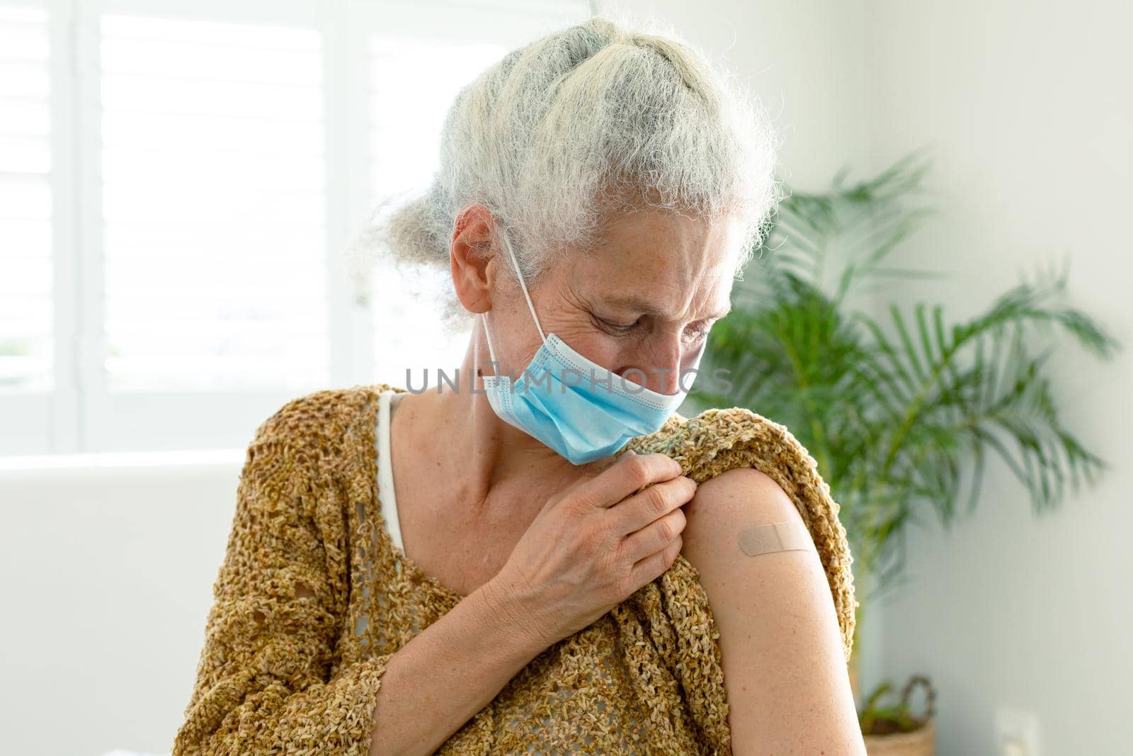 Smiling caucasian senior woman with plaster on arm after vaccination, wearing face mask by Wavebreakmedia
