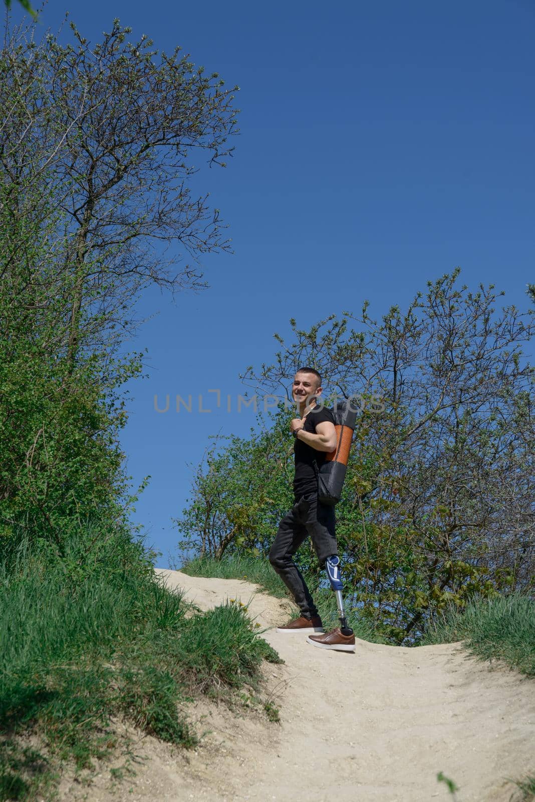 a man on a prosthetic leg travels the mountains. Dressed in black jeans and a T-shirt, he carrying mat.