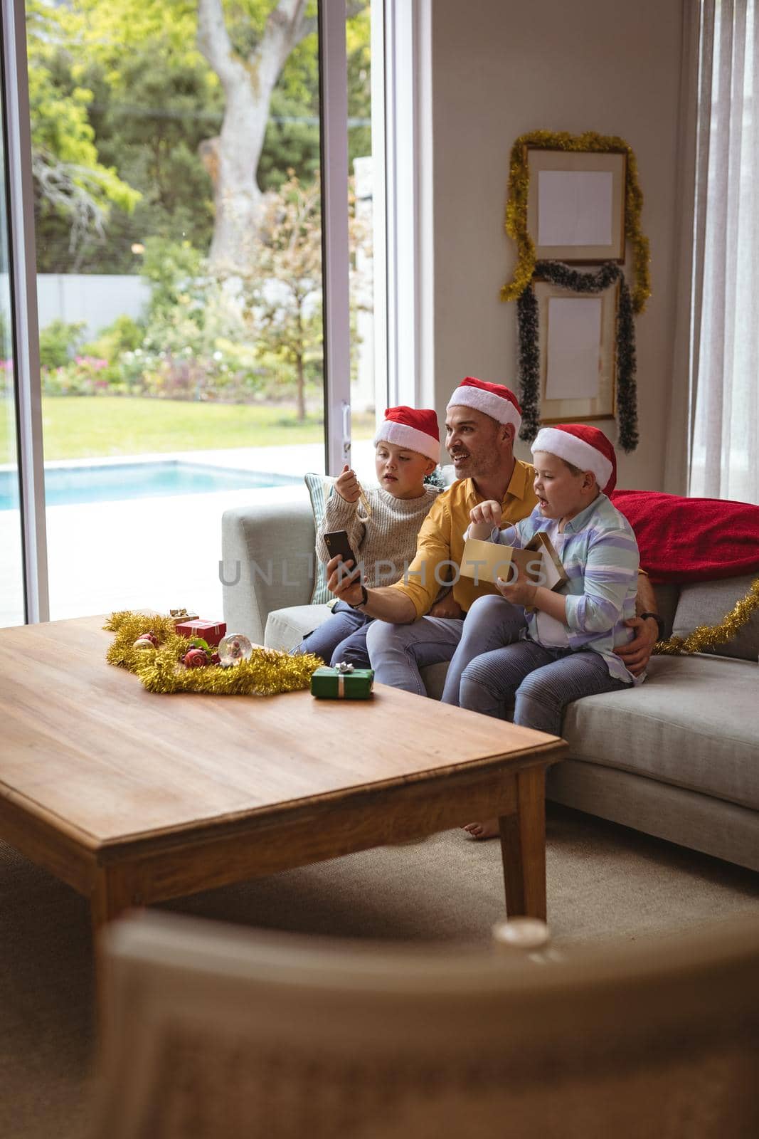 Caucasian father and two sons opening gift box during video call on smartphone during christmas. social distancing during covid 19 pandemic at christmas time