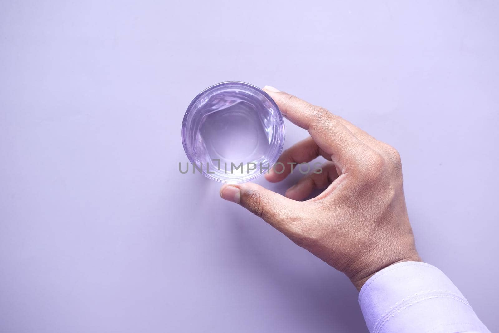 hand holding a glass of water on purple background .