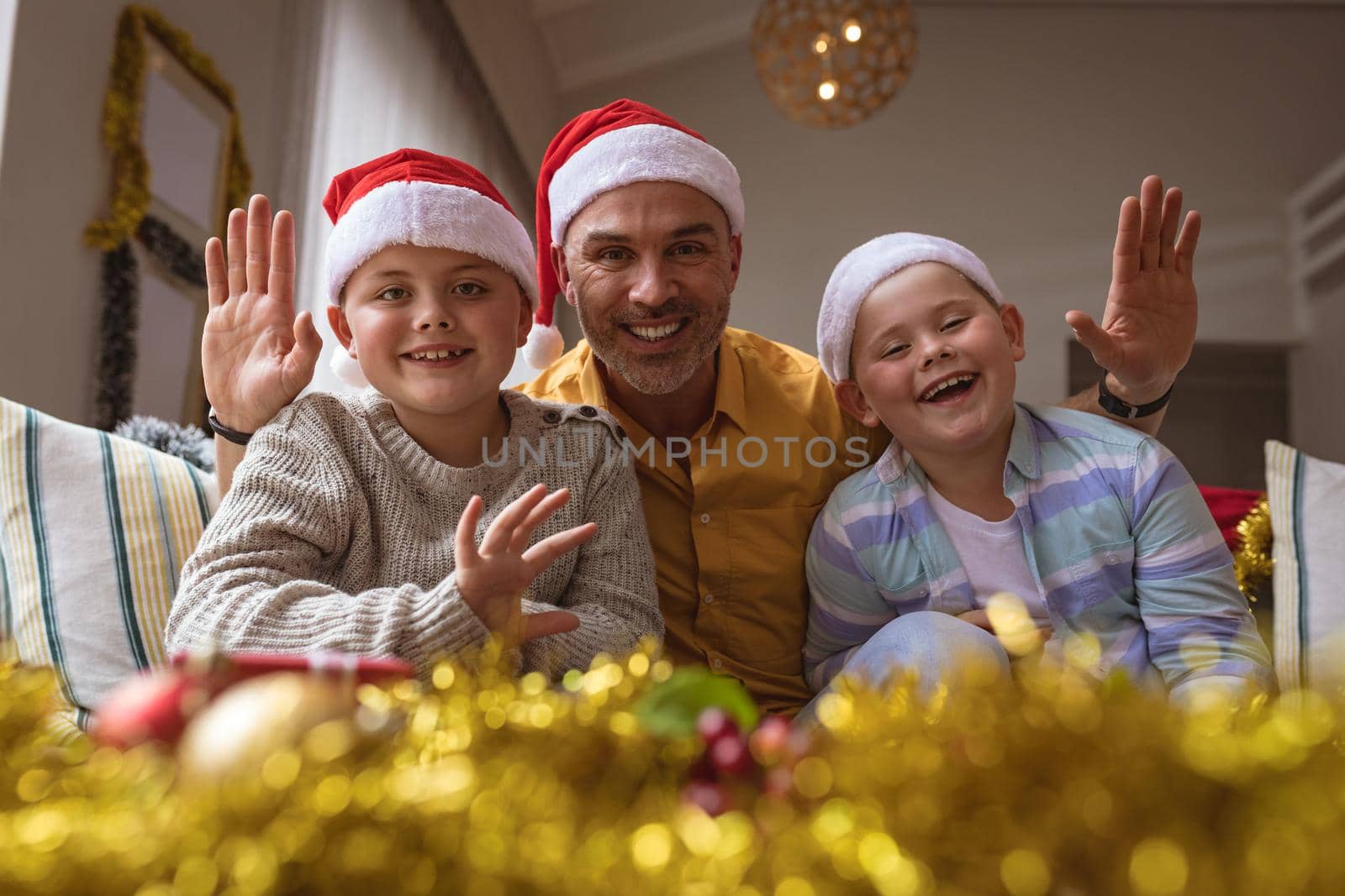Portrait of caucasian father and two sons smiling while sitting on couch at home during christmas. christmas festivity and celebration concept