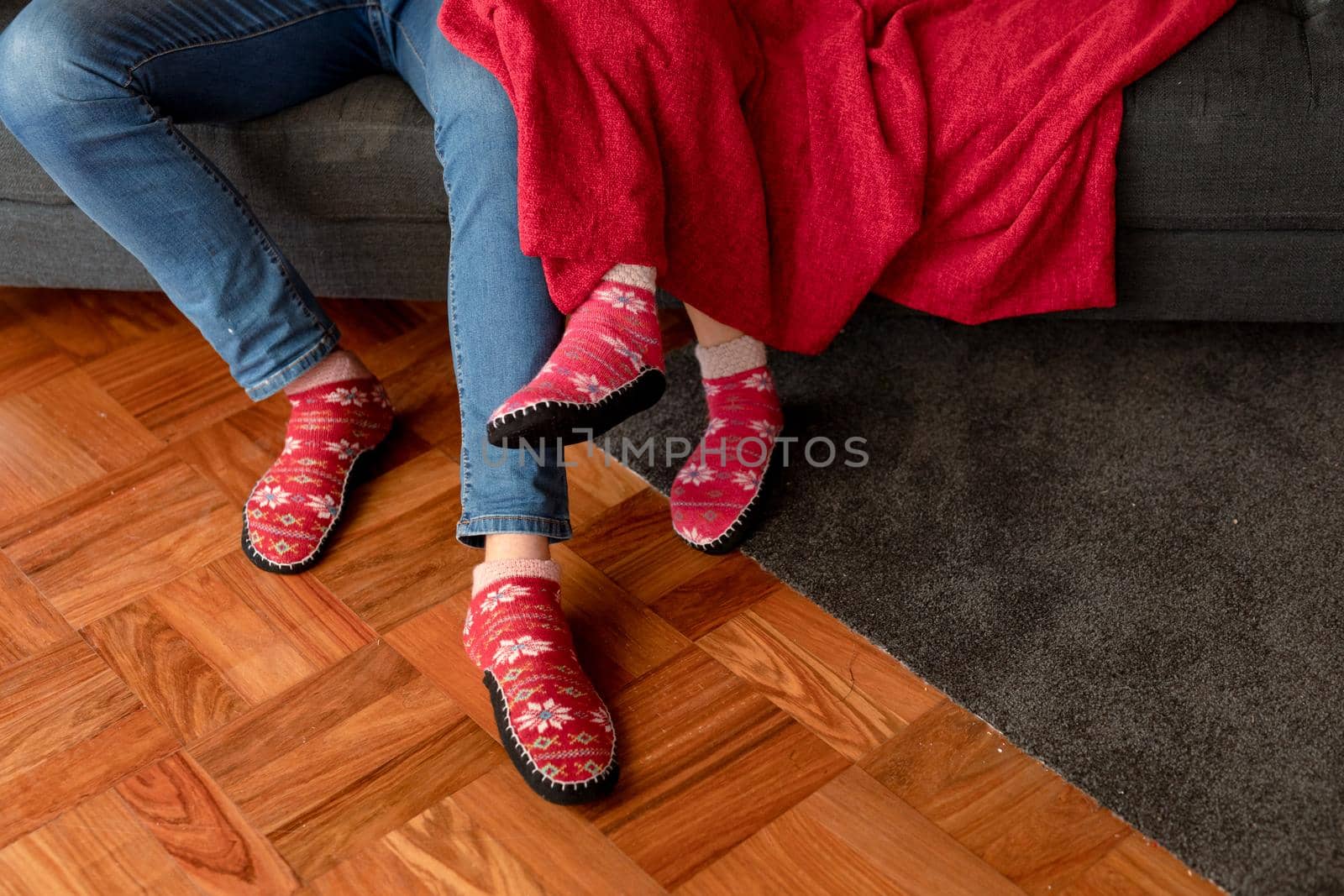 Legs of caucasian couple sitting on sofa with blanket in christmas socks. christmas, festivity and tradition at home.