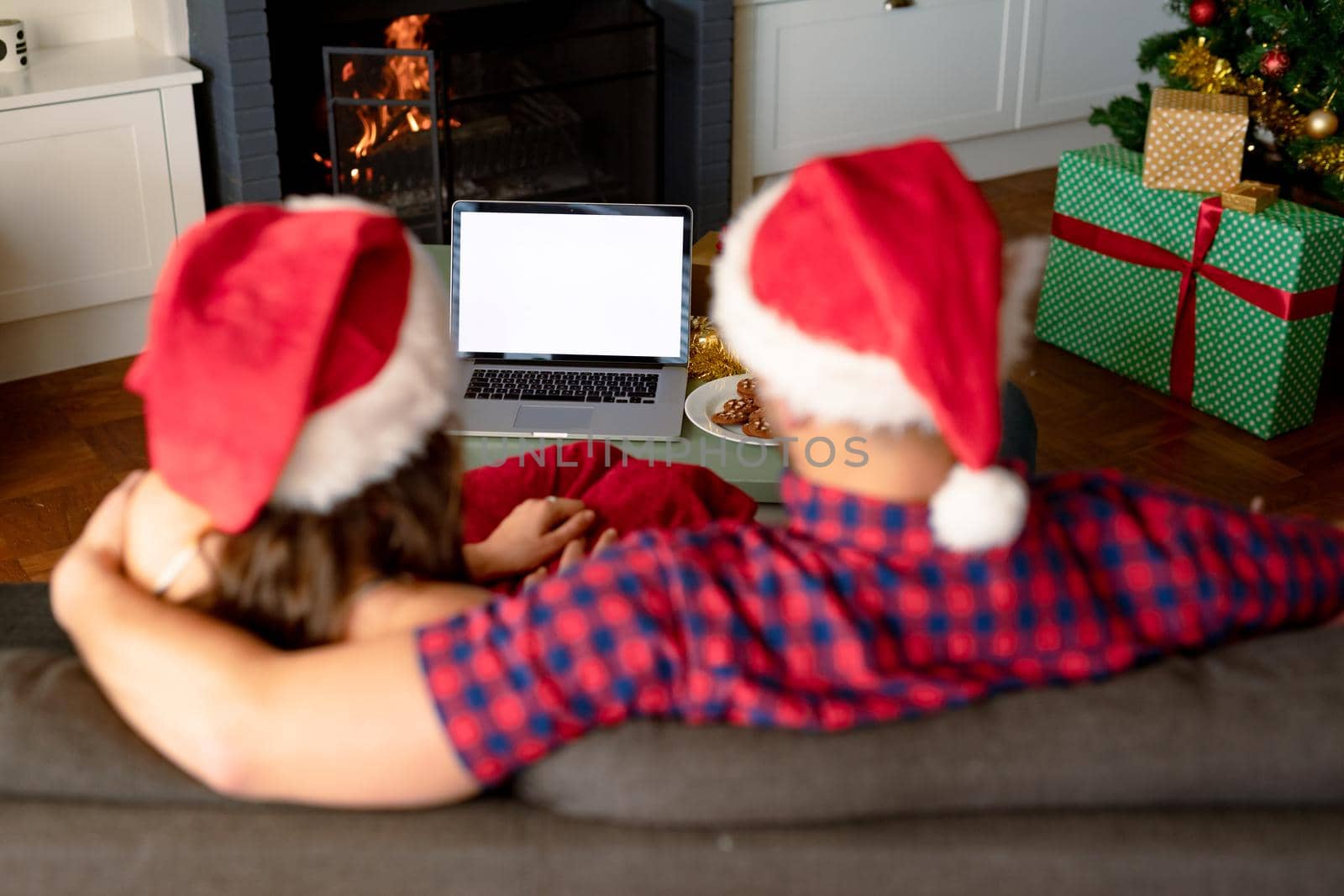 Back view of caucasian couple wearing santa hats, using laptop with copy space at christmas time. christmas, festivity and communication technology.