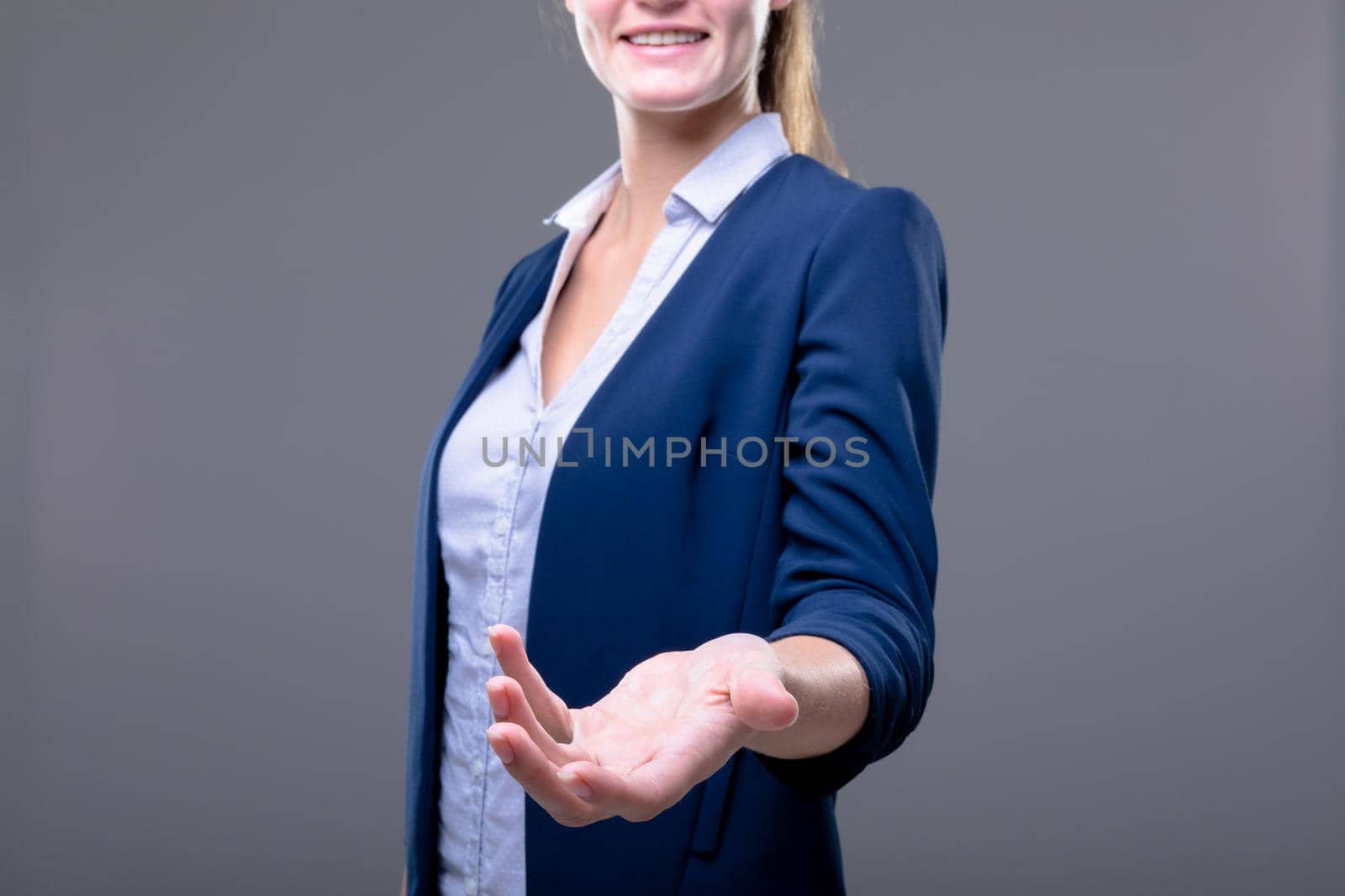 Smiling caucasian businesswoman reaching with her hand, isolated on grey background by Wavebreakmedia