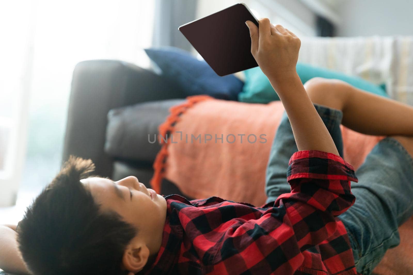 Asian boy using tablet with blank screen lying on floor at home. domestic lifestyle, leisure and technology during covid 19 pandemic concept.