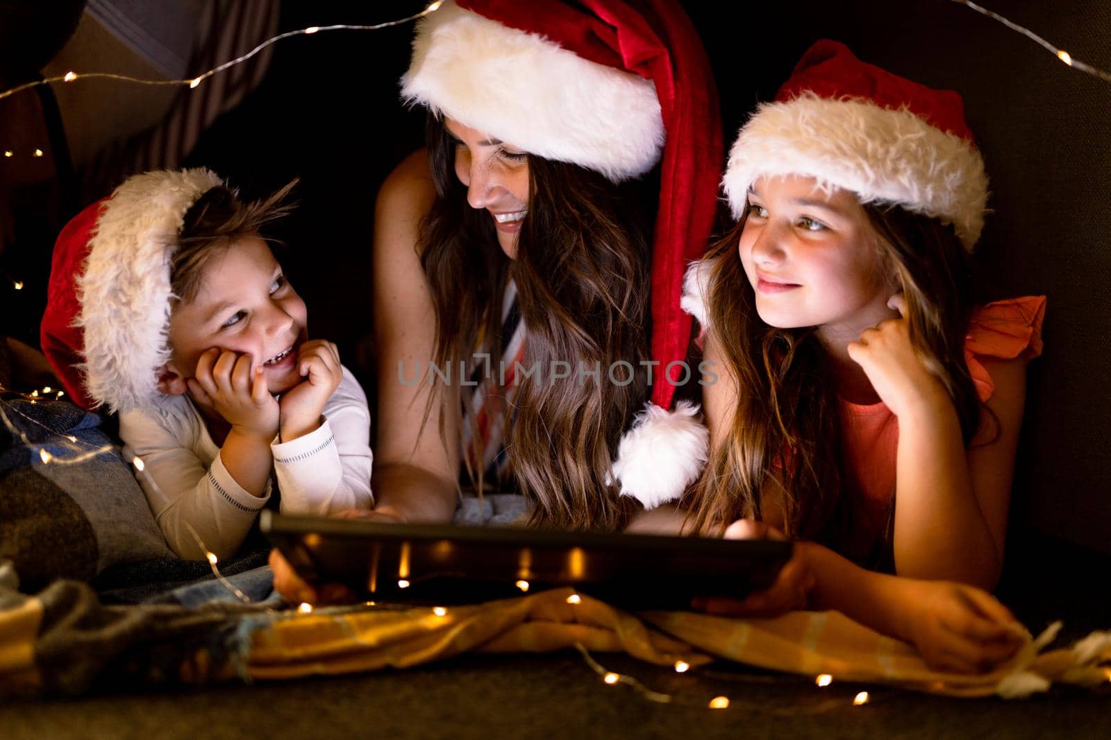 Happy caucasian mother, daughter and son wearing santa hats, using tablet at christmas time by Wavebreakmedia