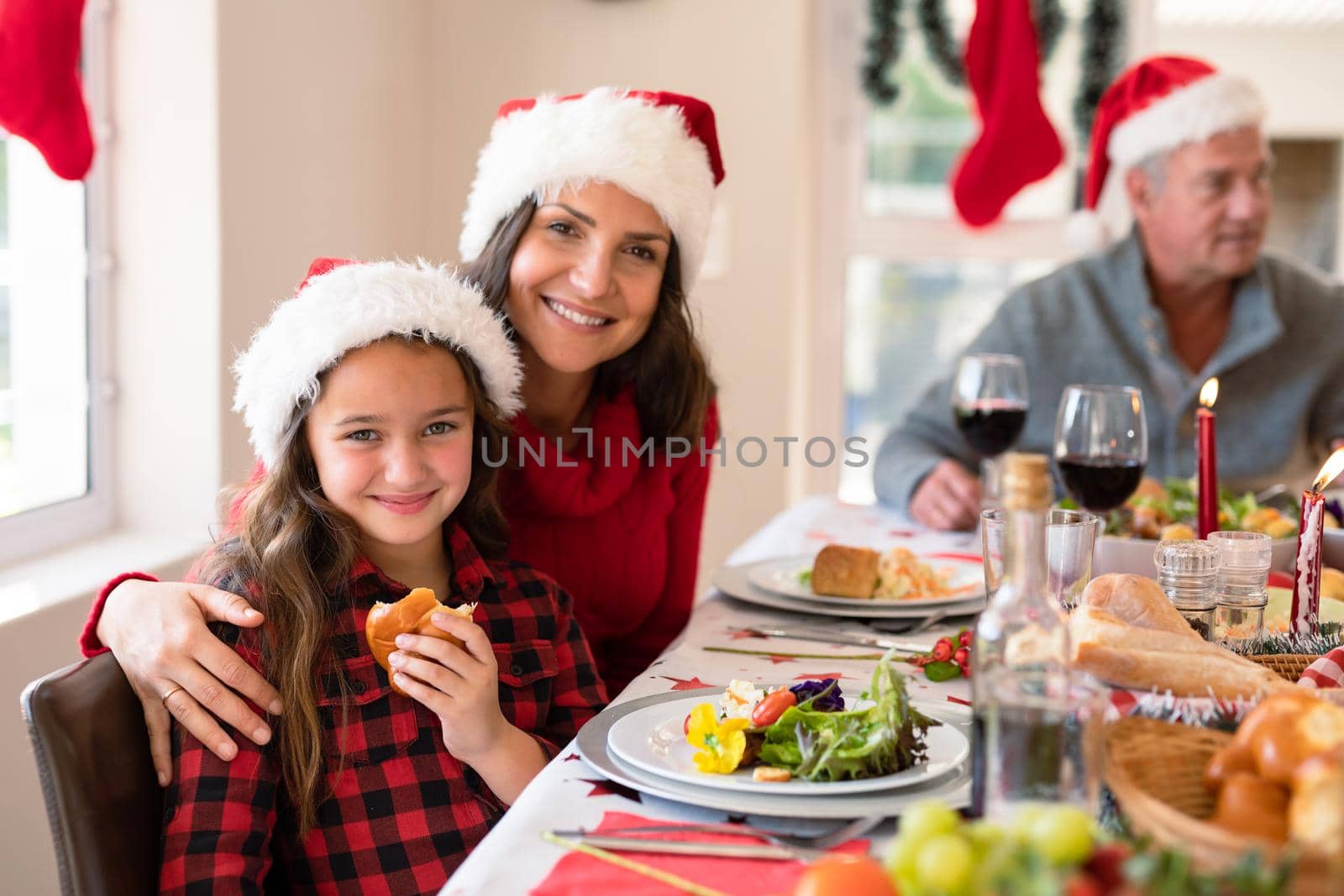 Happy caucasian mother and daughter wearing santa hats looking at camera at christmas time by Wavebreakmedia