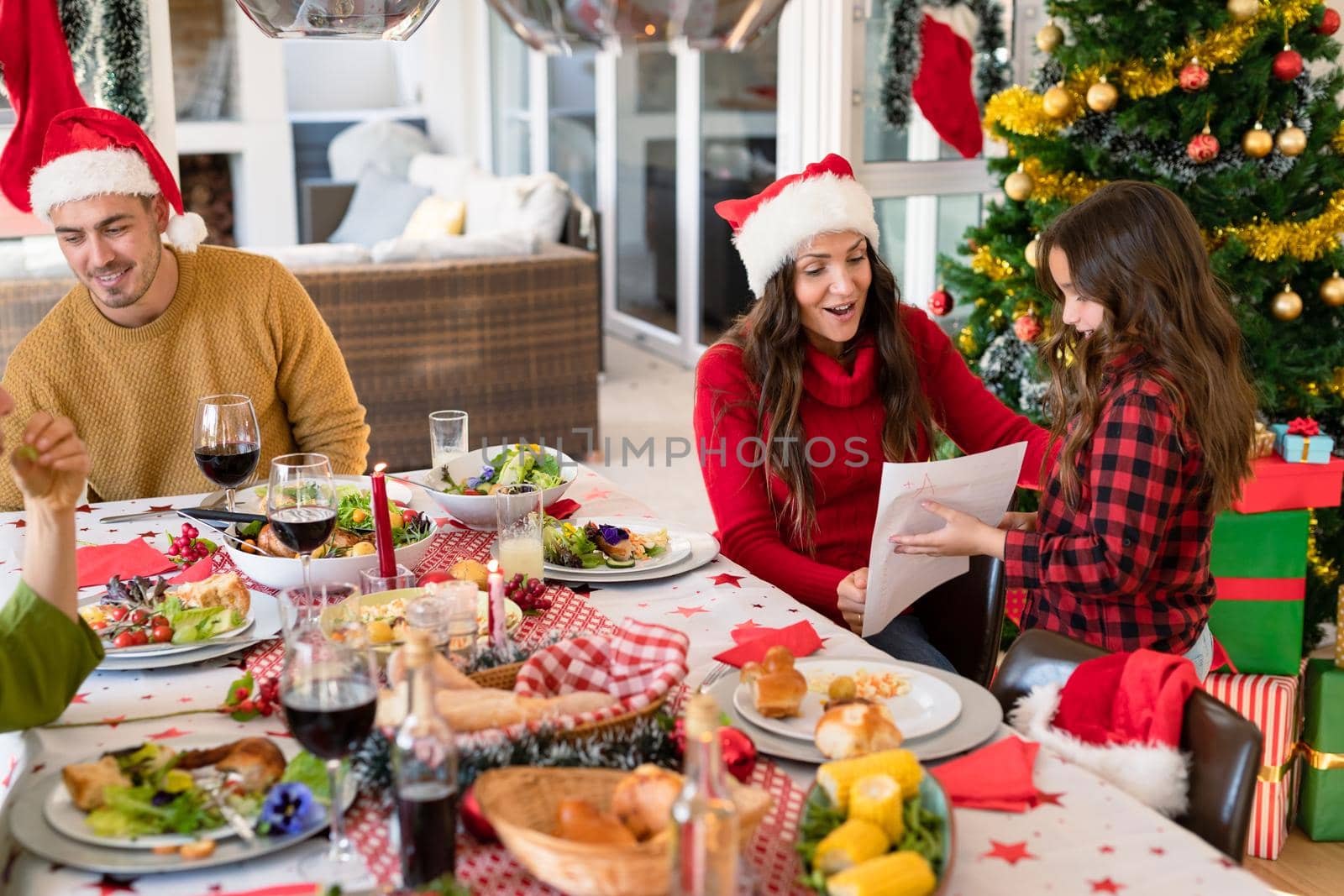 Happy and proud caucasian parents looking at their daughter diploma at christmas time. christmas time and festivity together at home.
