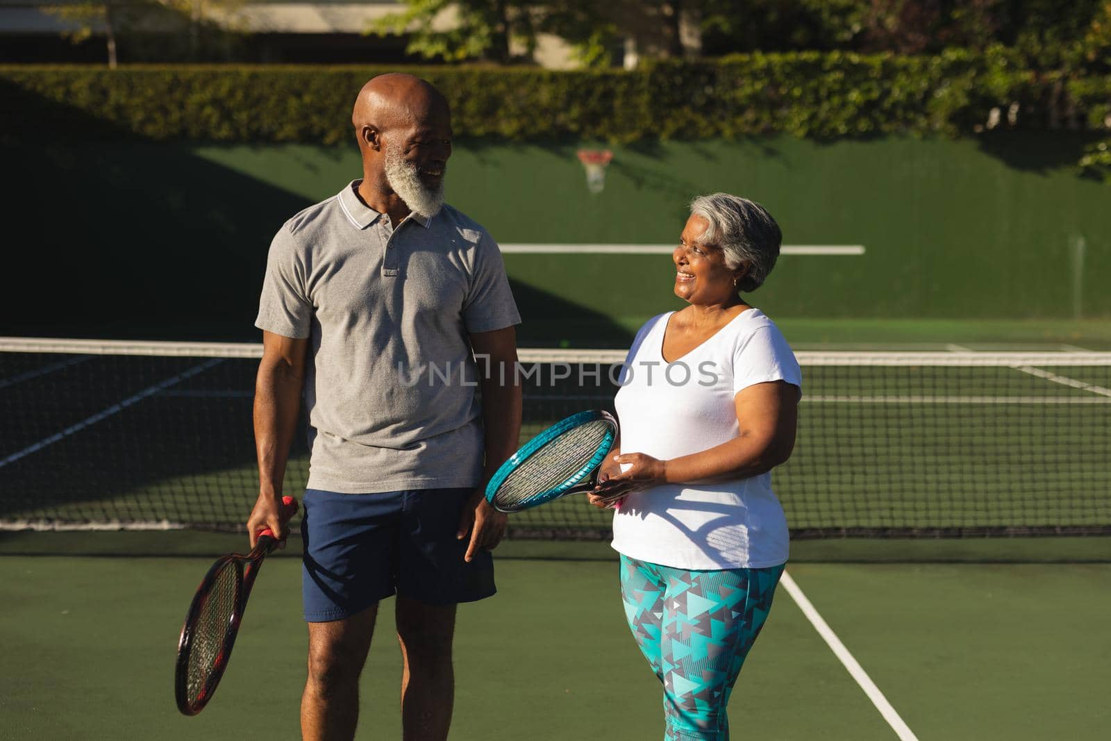 Portrait of smiling senior african american couple with tennis rackets on tennis court. retirement and active senior lifestyle concept.