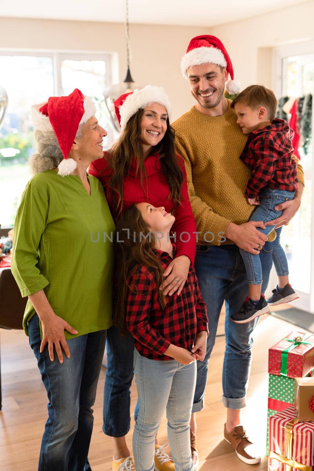 Happy multi generation caucasian family wearing santa hats taking photo at christmas time. christmas time and festivity together at home.