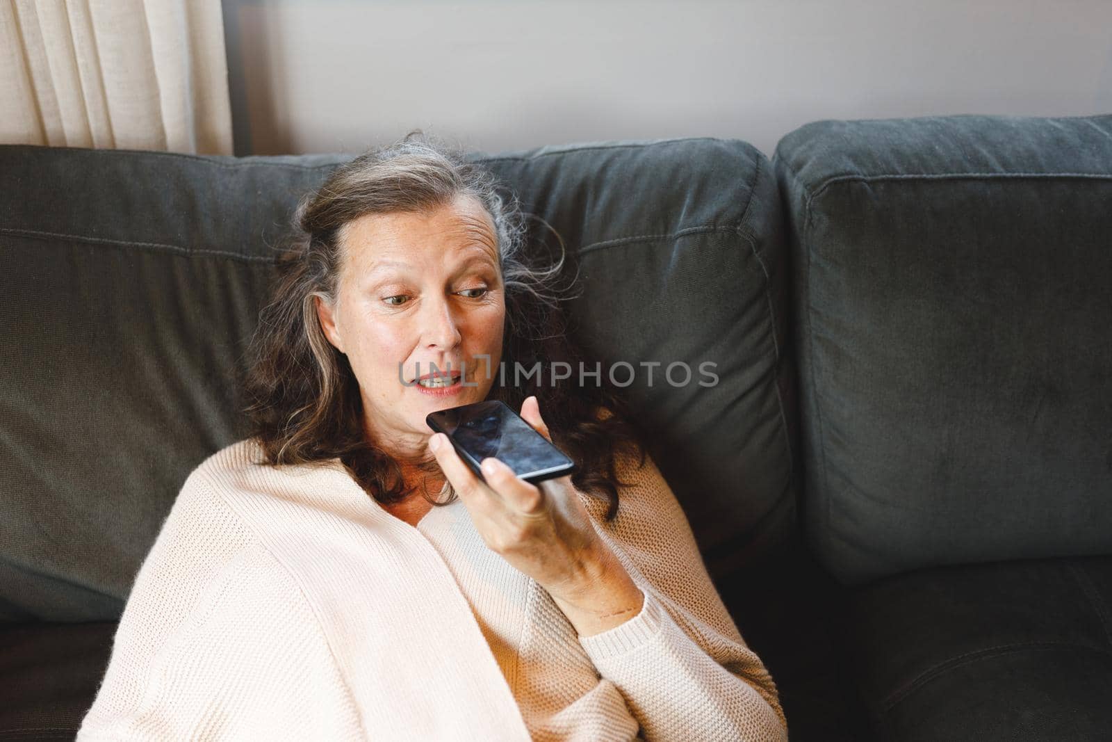 Happy senior caucasian woman in living room sitting on sofa, talking on smartphone. retirement lifestyle, spending time alone at home with technology.