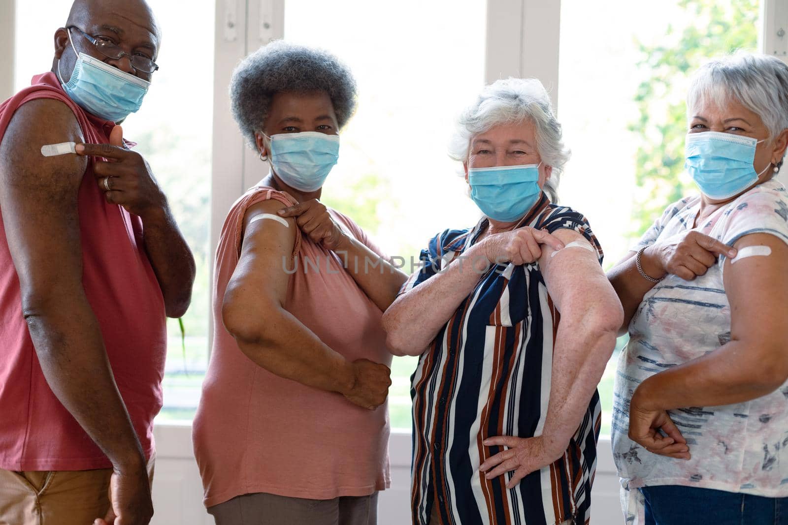 Four diverse male and female senior friends wearing face masks showing plasters after vaccination. senior health and lifestyle during covid 19 pandemic.