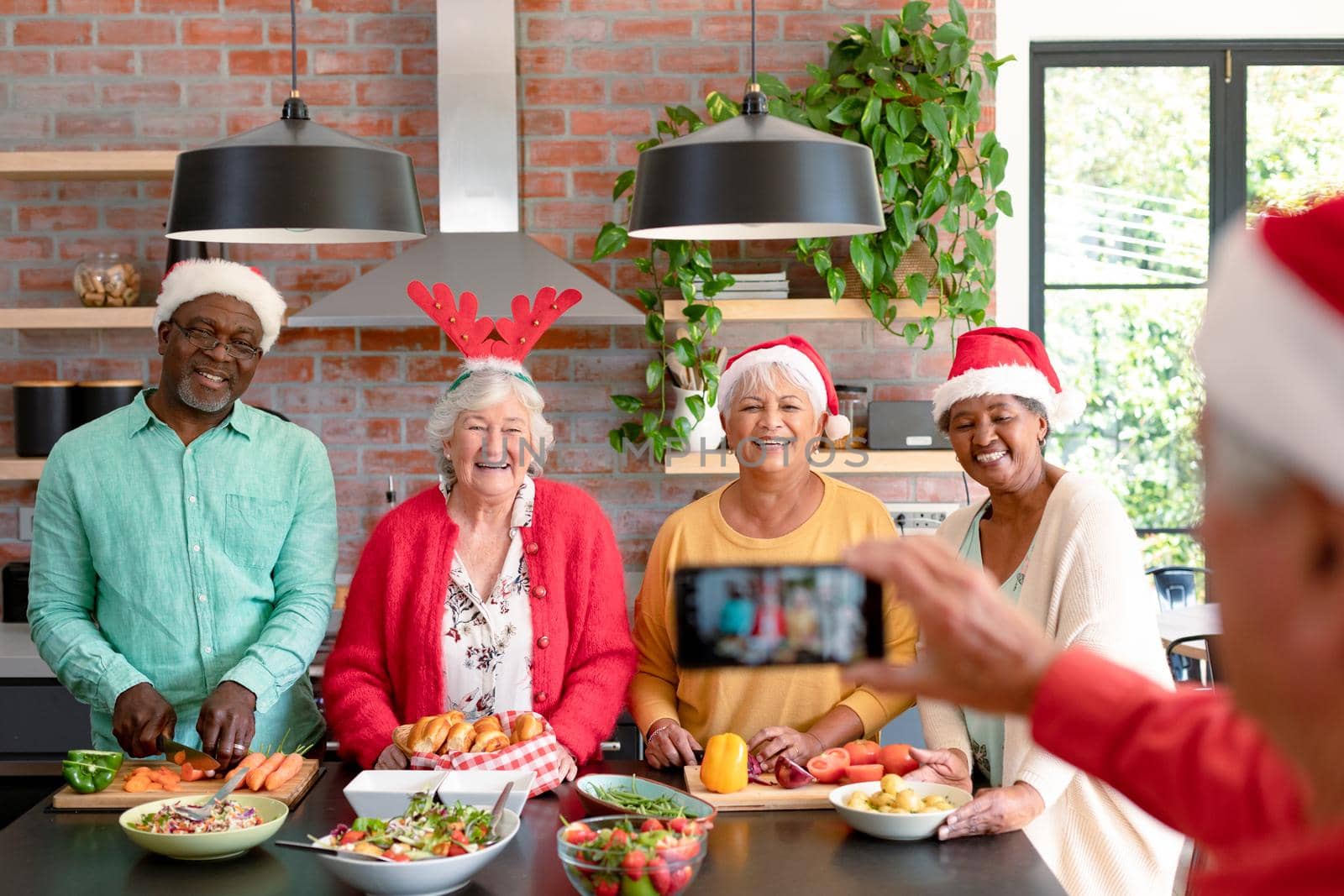 Group of happy diverse senior male and female friends in christmas hats taking selfie in kitchen by Wavebreakmedia