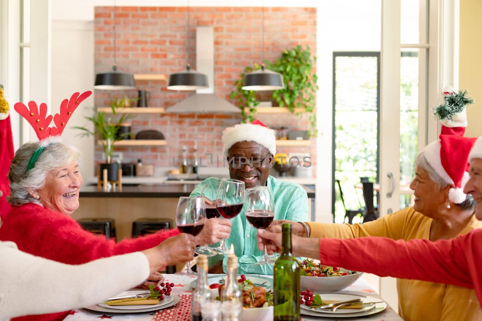 Diverse group of happy senior friends celebrating christmas with vine together at home by Wavebreakmedia