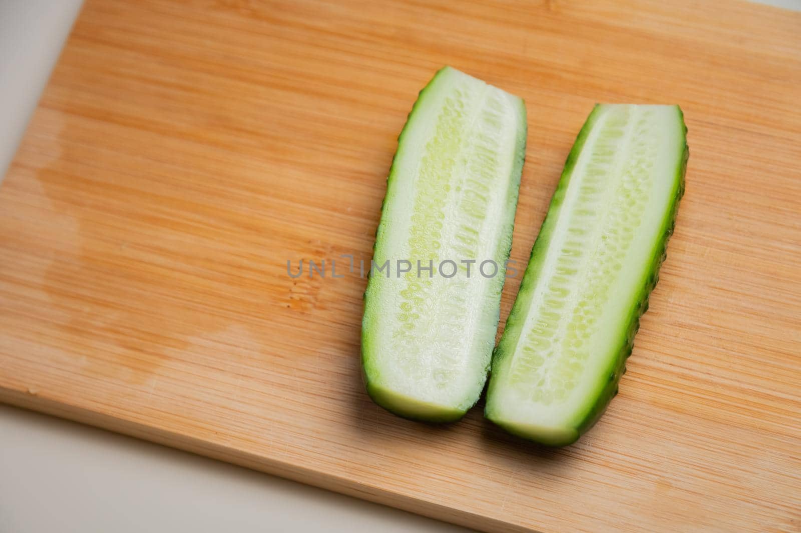 juicy ripe cucumber cut in half lies on a wooden cutting board. top view, shooting on the table.