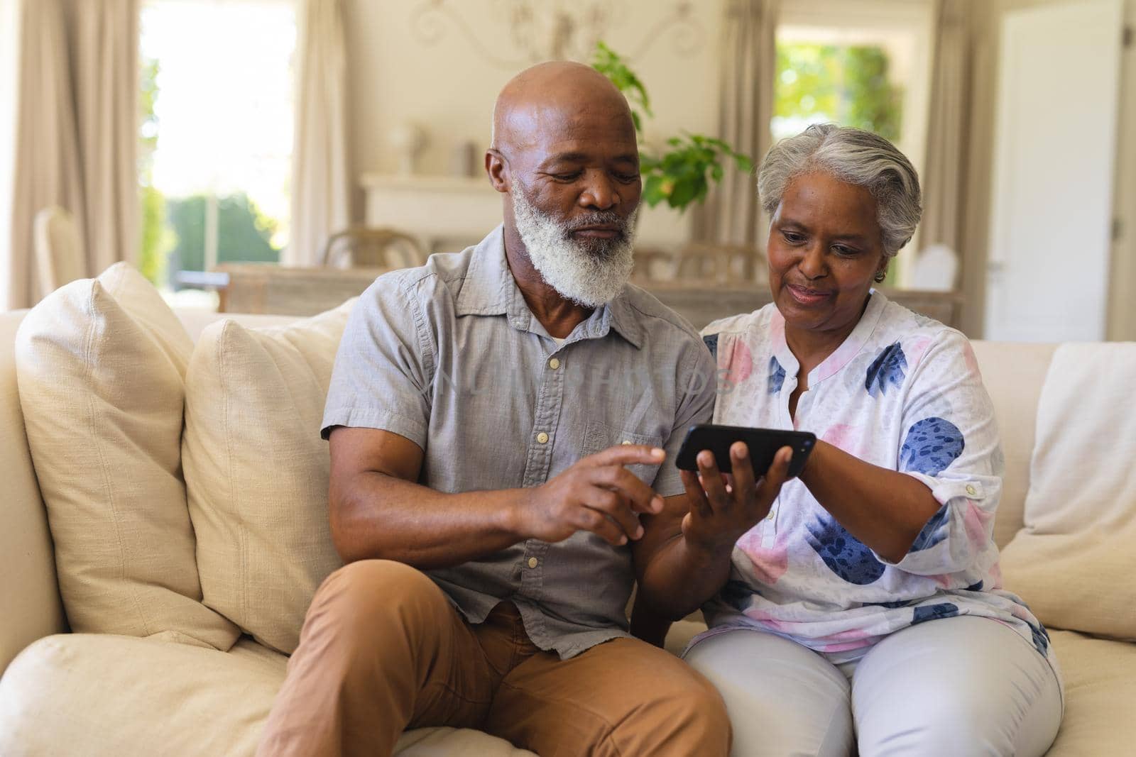 Senior african american couple sitting on sofa using smartphone. retreat, retirement and happy senior lifestyle concept.