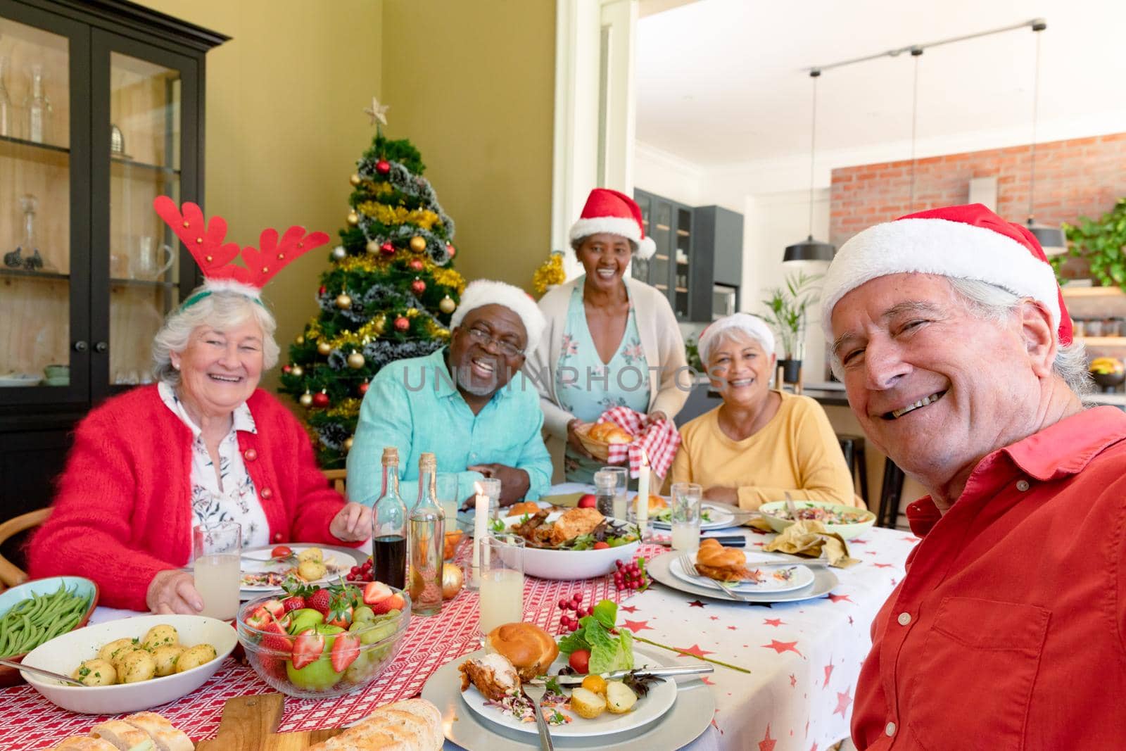Diverse group of happy senior friends in holiday hats celebrating christmas together, taking selfie. christmas festivities, celebrating at home with friends.