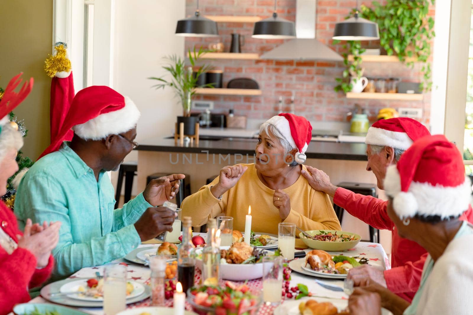 Diverse group of happy senior friends in holiday hats celebrating christmas together at home by Wavebreakmedia