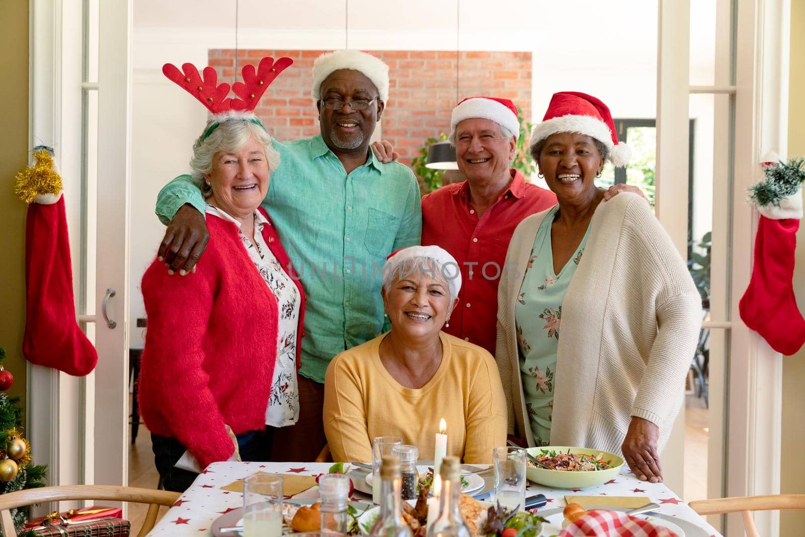Diverse group of happy senior friends in holiday hats celebrating christmas together, taking photo. christmas festivities, celebrating at home with friends.