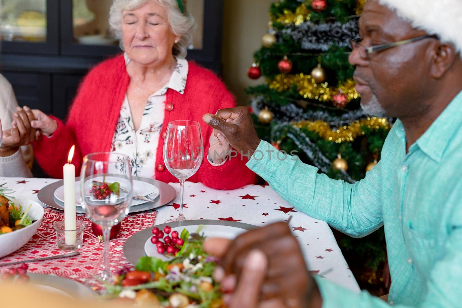 Diverse group of happy senior friends praying, celebrating christmas together at home by Wavebreakmedia