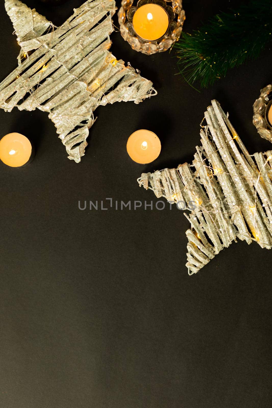 Composition of candles with tree branches, stars and copy space on black background. christmas, tradition and celebration concept.
