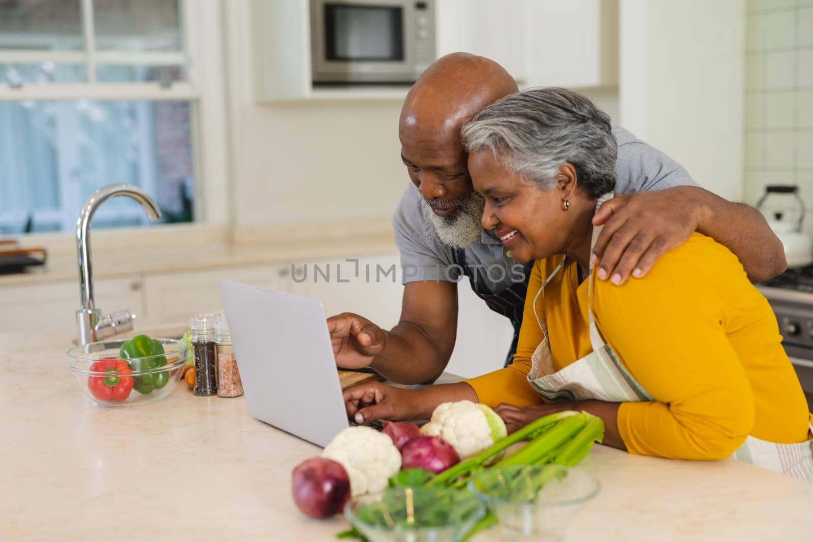 Senior african american couple cooking together in kitchen using laptop. retreat, retirement and happy senior lifestyle concept.