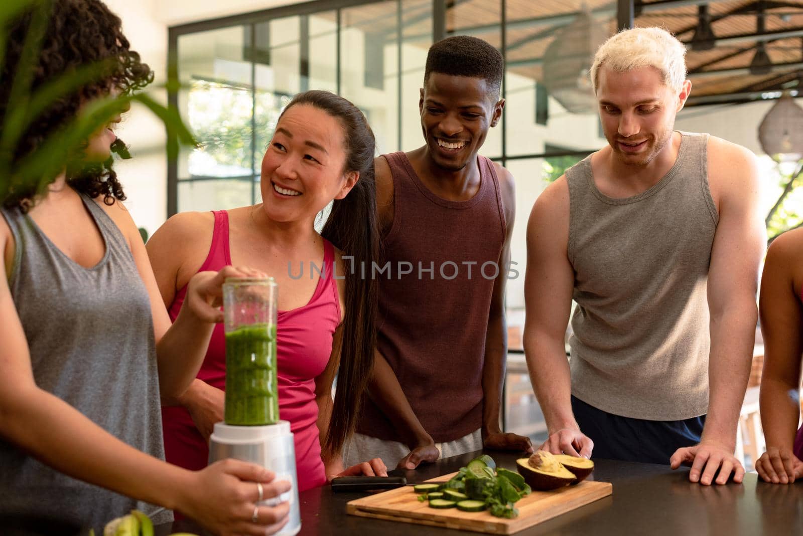 Group of diverse female and male friends preparing smoothie together in kitchen. fitness and healthy, active lifestyle.